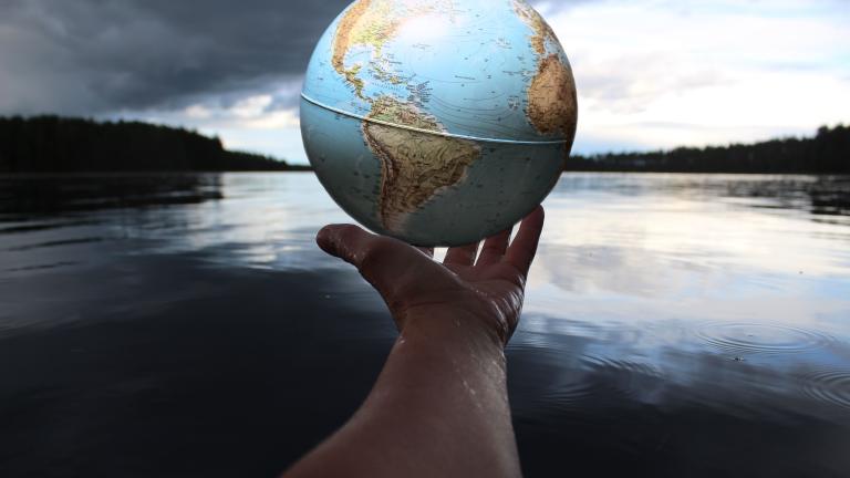 A person holding a globe over a body of water.