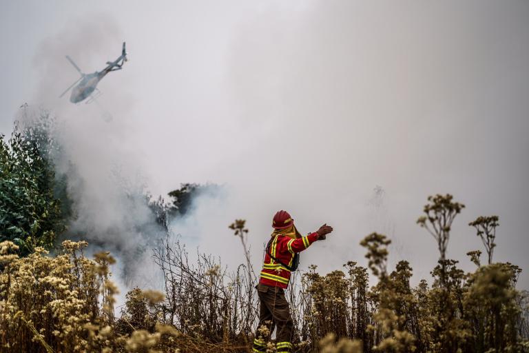 A firefighter is standing in a field near a helicopter.